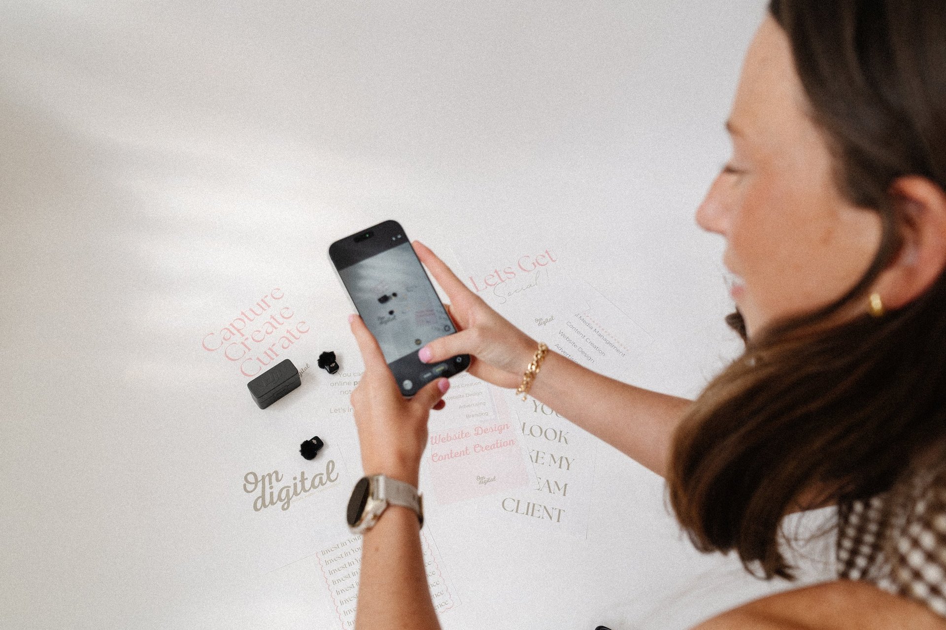 Woman holding smartphone displaying design mockup, standing in front of whiteboard with sketches and text